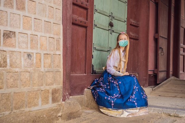 韓服の民族衣装を着た医療用マスクを着た若い白人女性観光客が韓国に旅行する