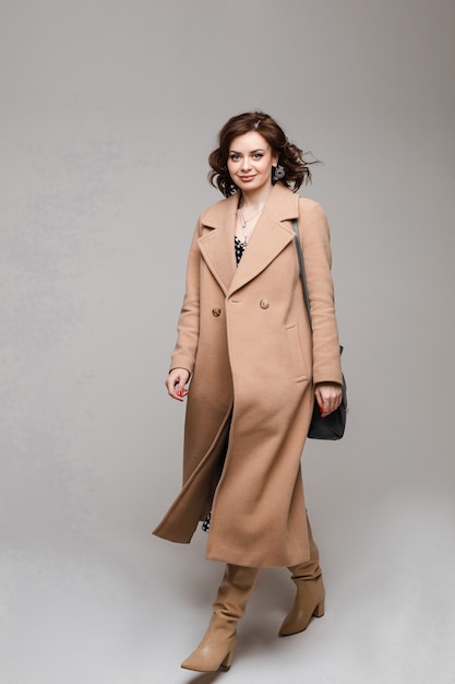 Young caucasian female with short chestnut wavy hair in long brown coat goes to home