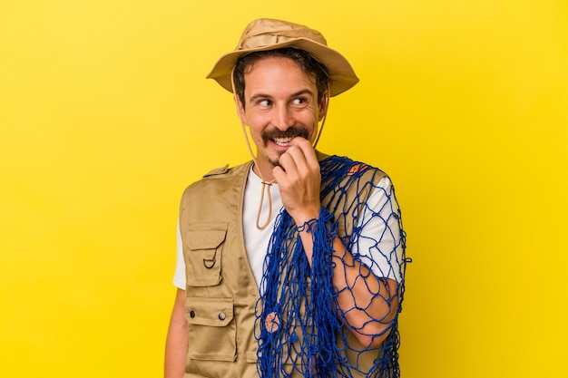 Young caucasian fisherman holding net isolated on yellow background relaxed thinking about something looking at a copy space