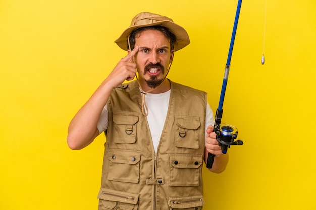 Young caucasian fisherman holding rod isolated on yellow background showing a disappointment gesture with forefinger.