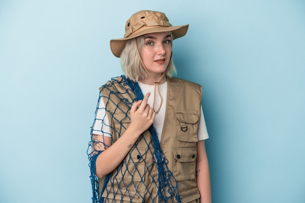 Young caucasian fisherwoman holding a net isolated on blue background pointing with finger at you as if inviting come closer.