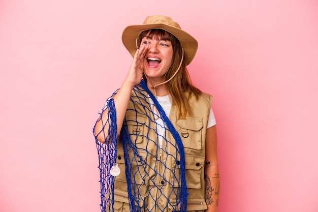 Young caucasian fisherwoman holding net isolated on blue background shouting and holding palm near opened mouth.