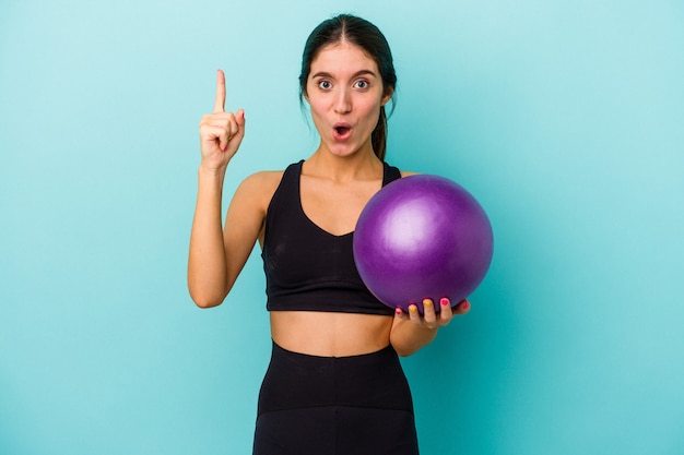 Young caucasian fitness woman holding a ball isolated on blue background having some great idea, concept of creativity.