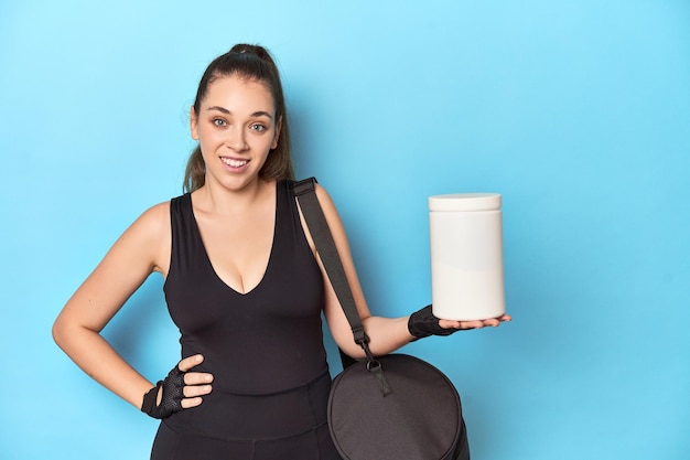 Young caucasian fitness woman holding a protein powder bottle isolated