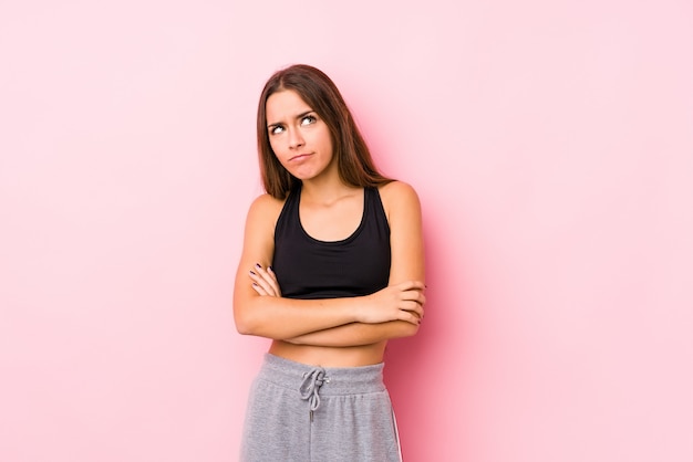 Young caucasian fitness woman posing in a pink background tired of a repetitive task.