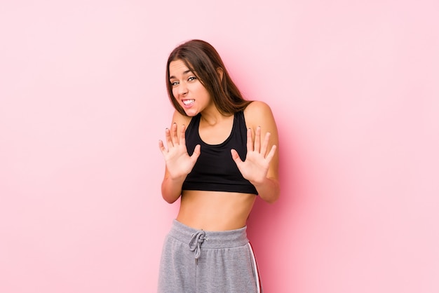 Молодая кавказская женщина фитнеса представляя в розовой стене отвергая кто-то показывая жест отвращения.