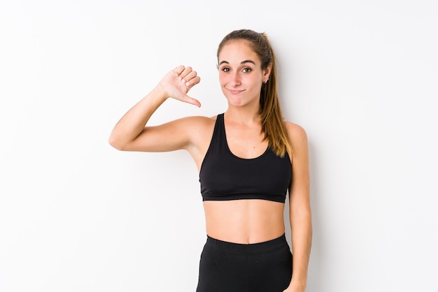 Young caucasian fitness woman posing in a white wall showing a dislike gesture, thumbs down. Disagreement concept.