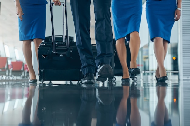 Giovani assistenti di volo caucasici con scarpe alla moda che camminano lungo il terminal dell'aeroporto