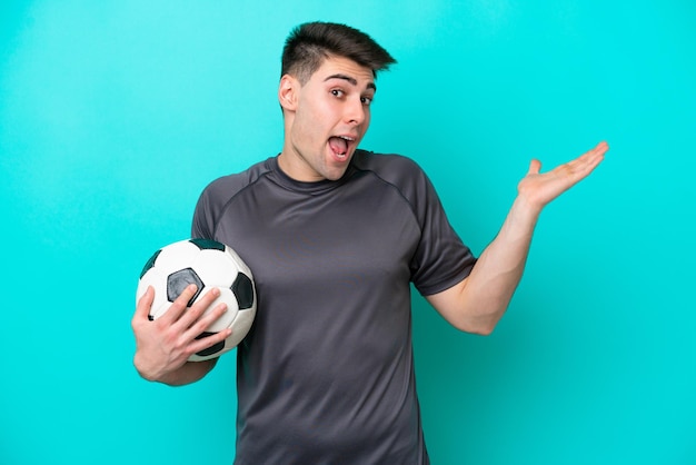 Young caucasian football player man isolated on blue background with shocked facial expression