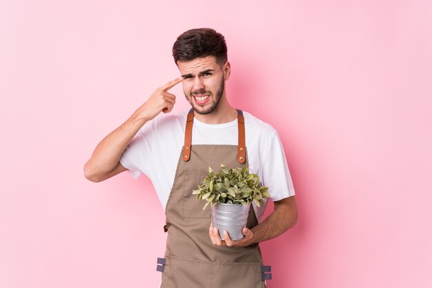 人差し指で失望のジェスチャーを示す分離された植物を保持している若い白人庭師男。