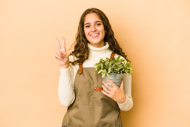 Young caucasian gardener woman holding a plant isolated showing number two with fingers.