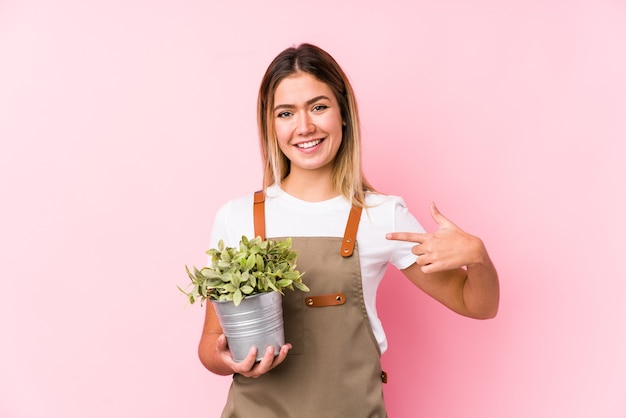 Young caucasian gardener woman in a pink background person pointing by hand to a shirt copy space, proud and confident