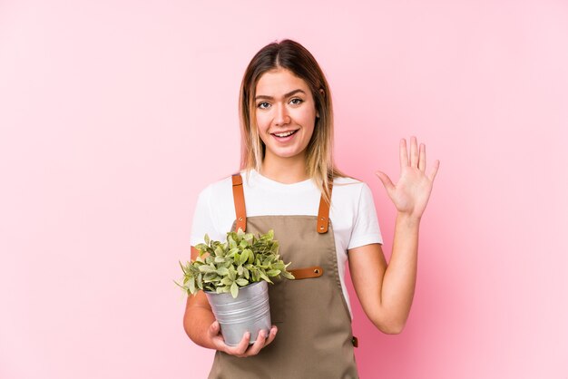ピンクの壁に若い白人の庭師の女性は、指で5番を示して陽気に笑っています。