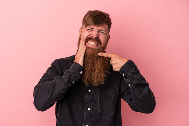 写真 強い歯の痛み、臼歯の痛みを持っているピンクの背景に分離された長いひげを持つ若い白人生姜男。