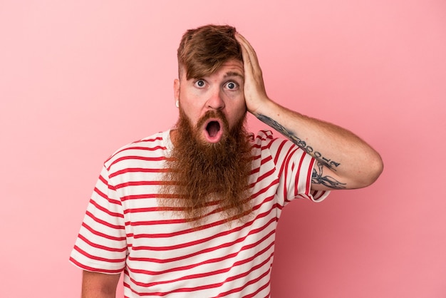 Young caucasian ginger man with long beard isolated on pink background being shocked, she has remembered important meeting.