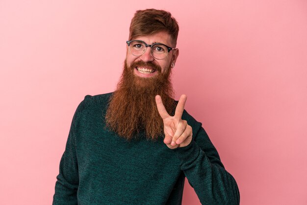 Photo young caucasian ginger man with long beard isolated on pink background joyful and carefree showing a peace symbol with fingers.