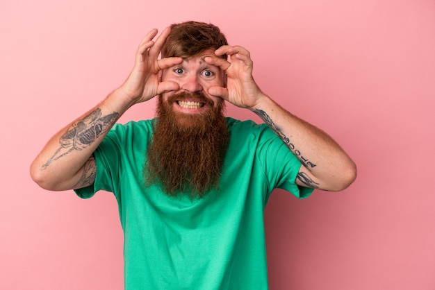 Young caucasian ginger man with long beard isolated on pink background keeping eyes opened to find a success opportunity.