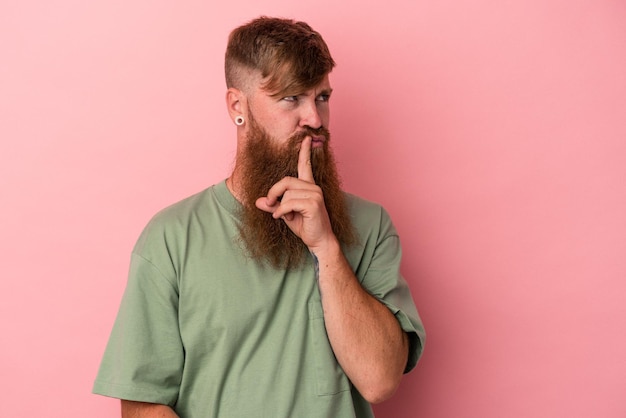 Young caucasian ginger man with long beard isolated on pink background looking sideways with doubtful and skeptical expression.