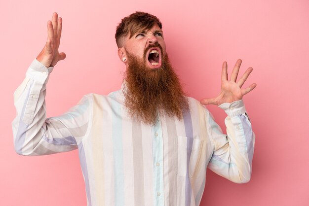 Foto giovane uomo caucasico di zenzero con barba lunga isolato su sfondo rosa che urla al cielo, alzando lo sguardo, frustrato.