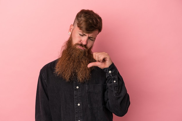 Young caucasian ginger man with long beard isolated on pink background showing a dislike gesture, thumbs down. Disagreement concept.