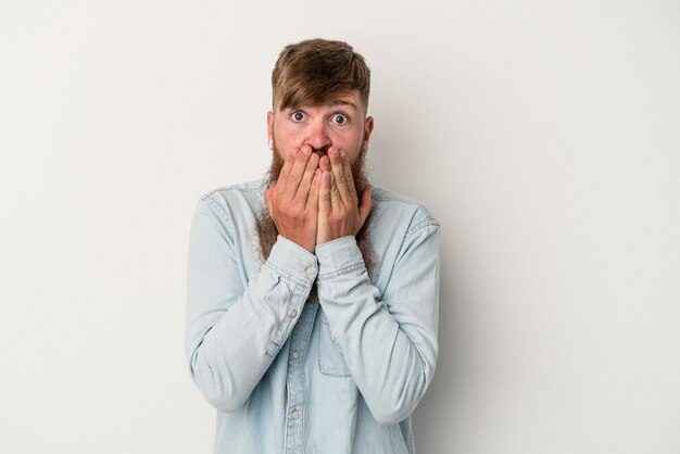 Young caucasian ginger man with long beard isolated on white background covering mouth with hands looking worried.