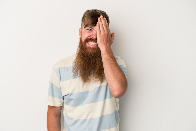 Young caucasian ginger man with long beard isolated on white background having fun covering half of face with palm.