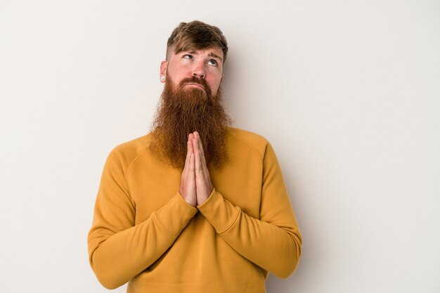 Young caucasian ginger man with long beard isolated on white background holding hands in pray near mouth, feels confident.