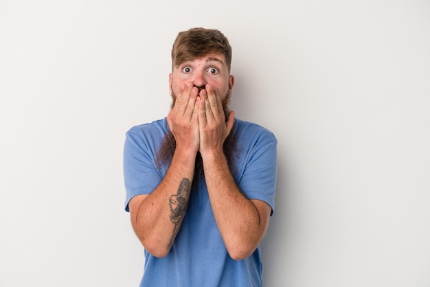 Young caucasian ginger man with long beard isolated on white background shocked covering mouth with hands.