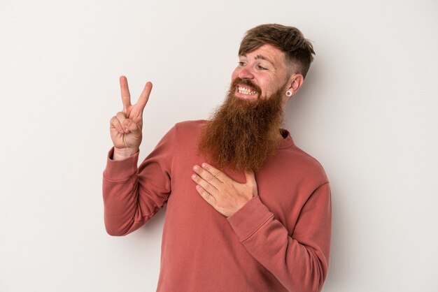 Giovane uomo caucasico di zenzero con la barba lunga isolato su sfondo bianco prestando giuramento, mettendo la mano sul petto.