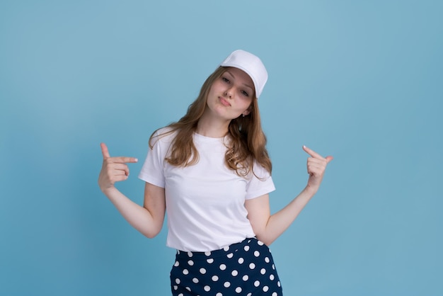 Young caucasian girl in delivery uniform and white cap looks confident with smile on her face pointi...