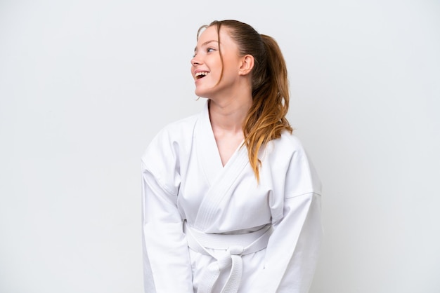 Young caucasian girl doing karate isolated on white background laughing in lateral position