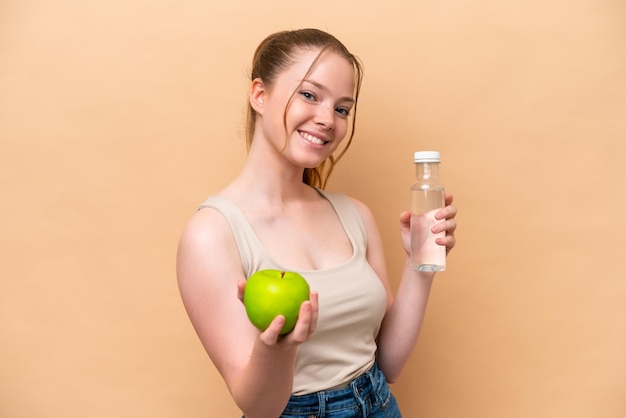 사과와 물 한 병으로 베이지색 배경에 고립 된 젊은 백인 소녀