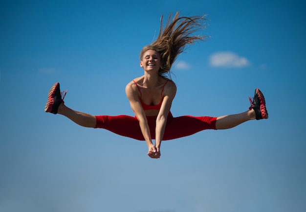 Фото Молодая кавказская девушка выполняет шпагат скача на backround неба.