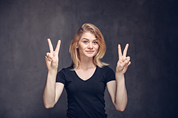 Young caucasian girl show victory sign on grey dark background