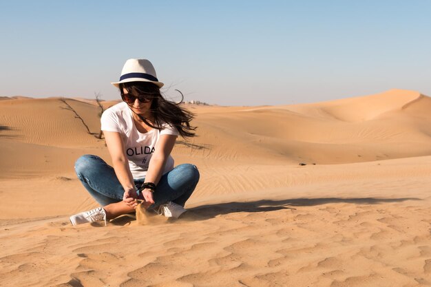 young caucasian girl sits on the sand in the desert in Abu Dhabi