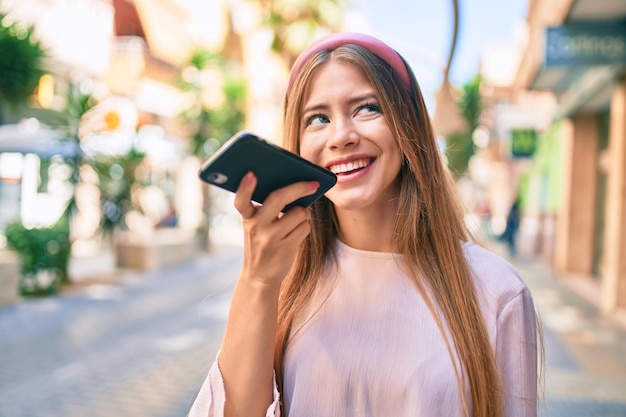 Young caucasian girl smiling happy sending audio message using smartphone at the city