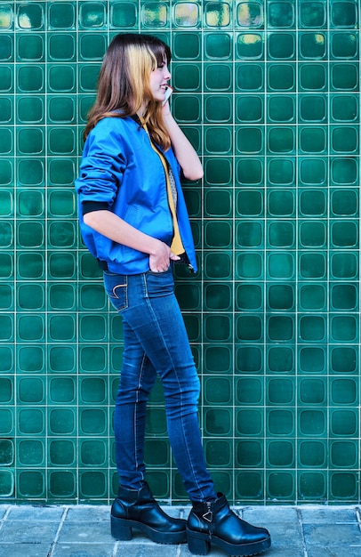 Foto giovane ragazza caucasica parlando al telefono cellulare su un muro verde in strada