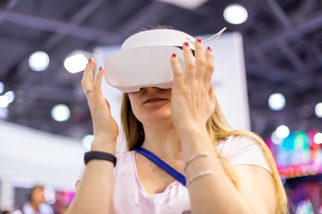 Young caucasian girl in a virtual reality helmet try to touch\
it. soft focus, bakground in blur