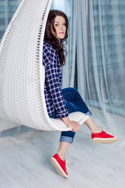 Young caucasian girl with dark curly hair wearing a blue plaid shirt, jeans and red sneakers.