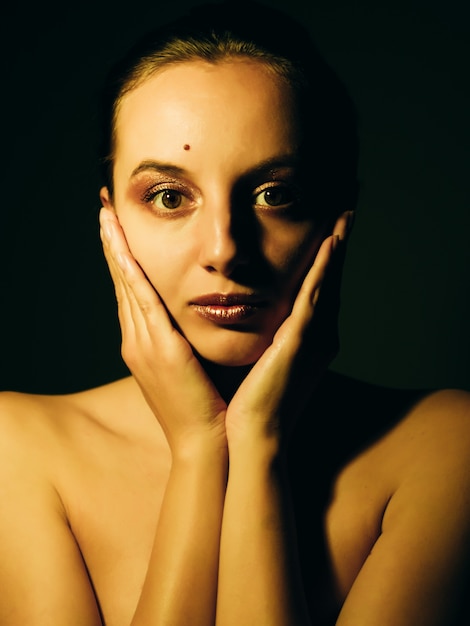 Young caucasian girl with golden make-up in the dark.