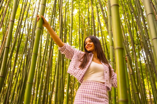 竹林にピンクのスカートをはいた白人少女熱帯気候の夏休みを楽しんで、竹の幹をつかんで森を散歩