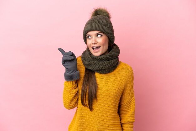 Young caucasian girl with winter hat isolated on pink background intending to realizes the solution while lifting a finger up