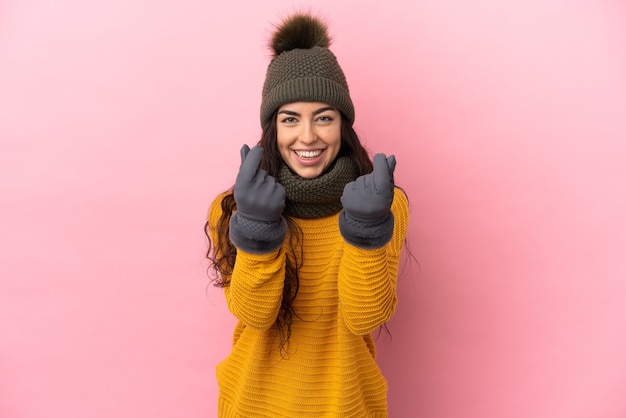 Giovane ragazza caucasica con cappello invernale isolato su sfondo viola che fa gesto di denaro