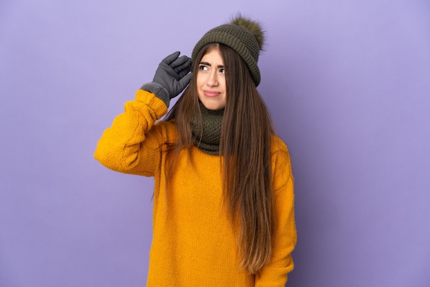 Young caucasian girl with winter hat isolated on purple wall having doubts