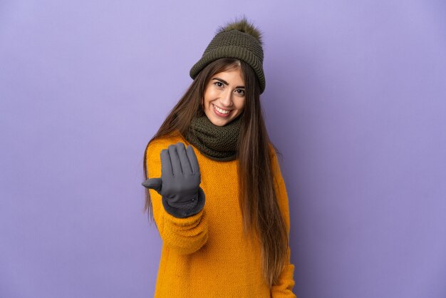 Young caucasian girl with winter hat isolated on purple wall inviting to come with hand. Happy that you came