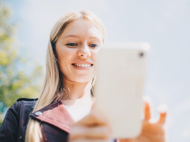 Young caucasian girl with wireless headphones in the park using tablet phone and smiling