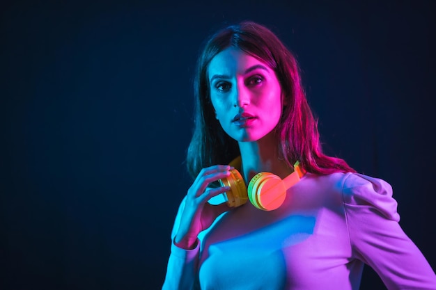 Young caucasian girl with yellow headphones on a black background, illuminated in a disco with neon lights