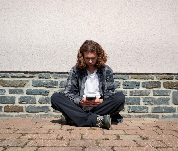 A young Caucasian guy sitting in his phone on the corner of the street