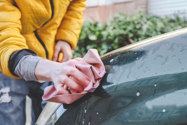 A young caucasian guy without a face in a yellow jacket rubs his hands with a pink rag and wipes the headlight