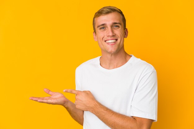 Young caucasian handsome man excited holding a copy space on palm.